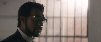 Movie still from “Come Sunday” (2018), directed by Joshua Marston – A person wearing glasses; Close Up shot, Over the shoulder angle
