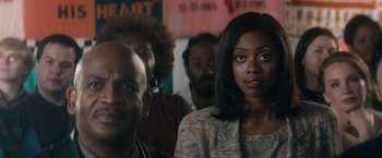 Movie still from “Come Sunday” (2018), directed by Joshua Marston – A group of people sitting in front of a wall; Close Up shot, Over the shoulder angle