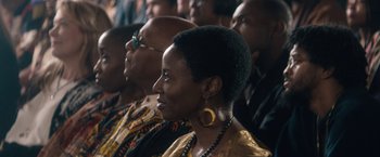 Movie still from “Come Sunday” (2018), directed by Joshua Marston – A group of people that are sitting in a room; Close Up shot, Over the shoulder angle