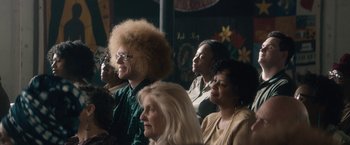 Movie still from “Come Sunday” (2018), directed by Joshua Marston – A group of people sitting next to each other in a room; Medium shot, Over the shoulder angle
