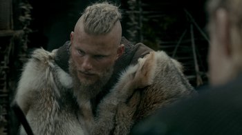 Movie still from “Vikings” (2013), created by Michael Hirst – A man with a beard is wearing a fur coat; Close Up shot, Over the shoulder angle
