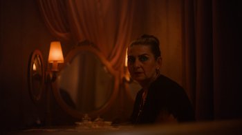 Movie still from “Copenhagen Cowboy” (2022), created by Nicolas Winding Refn – A woman sitting in front of a mirror in a dimly - lit room; Close Up shot, Over the shoulder angle