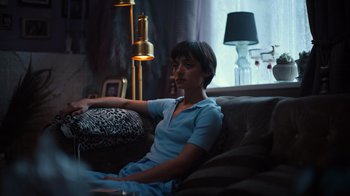 Movie still from “Copenhagen Cowboy” (2022), created by Nicolas Winding Refn – A person sitting on a couch in a living room; Medium shot, High angle