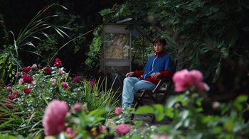 Movie still from “Copenhagen Cowboy” (2022), created by Nicolas Winding Refn – A man sitting on a chair in a garden; Wide shot, High angle