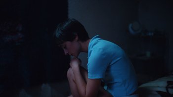 Movie still from “Copenhagen Cowboy” (2022), created by Nicolas Winding Refn – A woman sitting in a dark room with her head resting on her hand; Medium shot, High angle