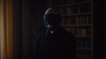 Movie still from “Copenhagen Cowboy” (2022), created by Nicolas Winding Refn – A man in a black robe with a mask on his face; Close Up shot, Over the shoulder angle