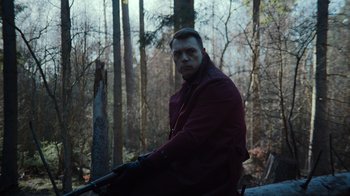 Movie still from “Copenhagen Cowboy” (2022), created by Nicolas Winding Refn – A man in a red jacket is holding a rifle; Medium shot, Low angle