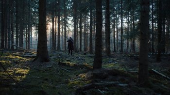 Movie still from “Copenhagen Cowboy” (2022), created by Nicolas Winding Refn – A person walking through the woods at sunset; Extreme Wide shot, Low angle