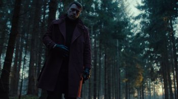 Movie still from “Copenhagen Cowboy” (2022), created by Nicolas Winding Refn – A man in a red coat standing in the woods; Medium shot, Low angle