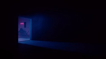 Movie still from “Copenhagen Cowboy” (2022), created by Nicolas Winding Refn – A dark room with a door open and a chair; Extreme Wide shot, Low angle