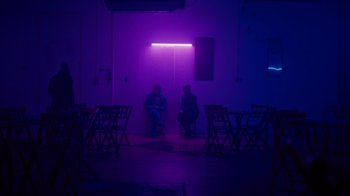 Movie still from “Copenhagen Cowboy” (2022), created by Nicolas Winding Refn – Two people sitting on chairs in a dark room; Wide shot, Over the shoulder angle