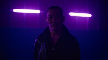Movie still from “Copenhagen Cowboy” (2022), created by Nicolas Winding Refn – A man standing in a room with purple lights; Medium shot, Low angle