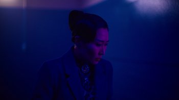 Movie still from “Copenhagen Cowboy” (2022), created by Nicolas Winding Refn – A woman in a dark room wearing a suit and tie; Close Up shot, Low angle
