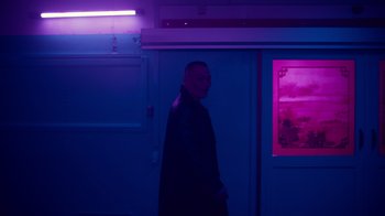 Movie still from “Copenhagen Cowboy” (2022), created by Nicolas Winding Refn – A man standing in front of a wall in a dark room; Medium shot, Over the shoulder angle