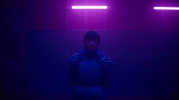 Movie still from “Copenhagen Cowboy” (2022), created by Nicolas Winding Refn – A person standing in front of a purple light; Medium shot, Low angle