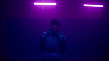 Movie still from “Copenhagen Cowboy” (2022), created by Nicolas Winding Refn – A person standing in a room lit by a purple light; Medium shot, Low angle