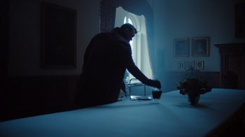 Movie still from “Copenhagen Cowboy” (2022), created by Nicolas Winding Refn – A man standing at a table in a dark room; Medium shot, Low angle