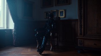Movie still from “Copenhagen Cowboy” (2022), created by Nicolas Winding Refn – A person sitting on a chair in a room; Wide shot, Low angle