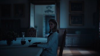 Movie still from “Copenhagen Cowboy” (2022), created by Nicolas Winding Refn – A woman sitting at a table with a glass of red wine; Medium shot, Low angle