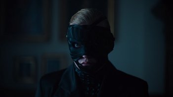 Movie still from “Copenhagen Cowboy” (2022), created by Nicolas Winding Refn – A man with a black mask on his face; Close Up shot, Low angle