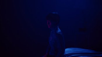 Movie still from “Copenhagen Cowboy” (2022), created by Nicolas Winding Refn – A person standing in a room lit by a blue light; Medium shot, High angle