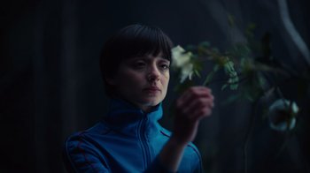 Movie still from “Copenhagen Cowboy” (2022), created by Nicolas Winding Refn – A woman in a blue jacket holding a flower; Close Up shot, Low angle