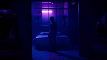 Movie still from “Copenhagen Cowboy” (2022), created by Nicolas Winding Refn – A man standing in front of a bed in a dark room; Wide shot, Low angle