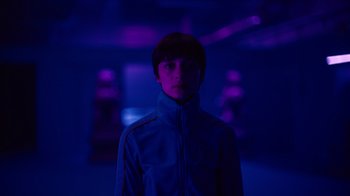 Movie still from “Copenhagen Cowboy” (2022), created by Nicolas Winding Refn – A man in a blue jacket standing in a dark room; Close Up shot, Low angle