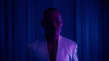 Movie still from “Copenhagen Cowboy” (2022), created by Nicolas Winding Refn – A man in a white jacket is in a purple room; Close Up shot, Low angle
