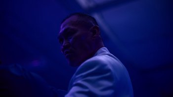 Movie still from “Copenhagen Cowboy” (2022), created by Nicolas Winding Refn – A man in a white jacket is standing in a dark room; Close Up shot, Low angle