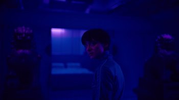 Movie still from “Copenhagen Cowboy” (2022), created by Nicolas Winding Refn – A person standing in a dark room with blue lighting; Medium shot, Over the shoulder angle