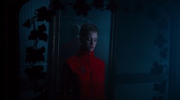 Movie still from “Copenhagen Cowboy” (2022), created by Nicolas Winding Refn – A woman in a red jacket standing in front of a mirror; Medium shot, Low angle