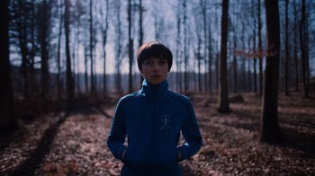 Movie still from “Copenhagen Cowboy” (2022), created by Nicolas Winding Refn – A person standing in the middle of a forest; Medium shot, Low angle