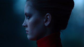Movie still from “Copenhagen Cowboy” (2022), created by Nicolas Winding Refn – A young woman in a red jacket looking to the side; Close Up shot, Low angle