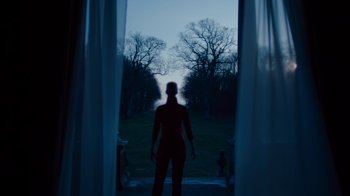 Movie still from “Copenhagen Cowboy” (2022), created by Nicolas Winding Refn – A man standing in front of a window at night; Wide shot, Low angle