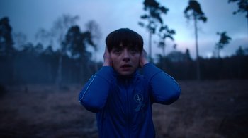 Movie still from “Copenhagen Cowboy” (2022), created by Nicolas Winding Refn – A person with their hands behind their ears; Close Up shot, Over the shoulder angle