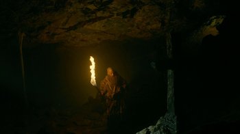 Movie still from “Vikings” (2013), created by Michael Hirst – A man in a cave holding a lit up stick; Wide shot, Low angle