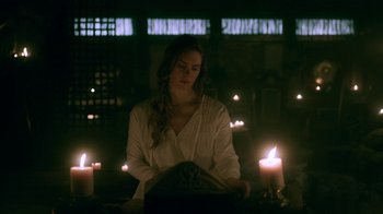 Movie still from “Vikings” (2013), created by Michael Hirst – A woman sitting in front of a computer in front of candles; Medium shot, Low angle