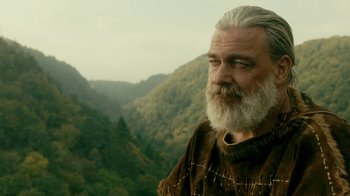 Movie still from “Vikings” (2013), created by Michael Hirst – An old man with a beard and a mustache is standing in front of a mountain range; Close Up shot, Low angle
