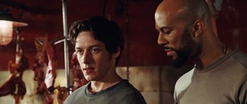 Movie still from “Wanted” (2008), directed by Timur Bekmambetov – A man standing next to another man in front of a brick wall; Close Up shot, Over the shoulder angle