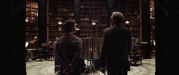 Movie still from “Wanted” (2008), directed by Timur Bekmambetov – Two men standing in front of a bookshelf in a library; Medium shot, Low angle