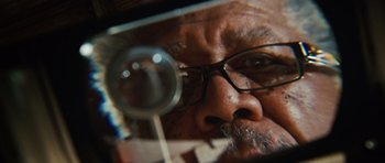 Movie still from “Wanted” (2008), directed by Timur Bekmambetov – An older man wearing glasses looking through a magnifying glass; Extreme Close Up shot, Overhead angle