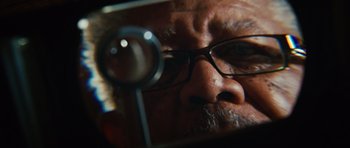 Movie still from “Wanted” (2008), directed by Timur Bekmambetov – An older man with glasses looking into a magnifying glass; Extreme Close Up shot, Low angle