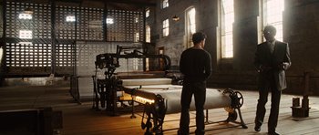 Movie still from “Wanted” (2008), directed by Timur Bekmambetov – A man standing in front of a machine in a room; Wide shot, Low angle