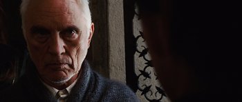 Movie still from “Wanted” (2008), directed by Timur Bekmambetov – An older man looking at the camera while a younger man takes a picture; Close Up shot, Over the shoulder angle