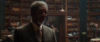 Movie still from “Wanted” (2008), directed by Timur Bekmambetov – An older man wearing a suit and tie in front of a book case; Medium shot, Over the shoulder angle