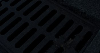 Movie still from “Cracow Monsters” (2022), created by Kasia Adamik – View of a metal grate in the dark; Extreme Close Up shot, Overhead angle