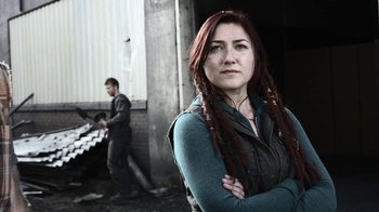 Movie still from “Z Nation” (2014), created by Karl Schaefer – A woman standing in front of a man with his hands crossed; Medium shot, Low angle