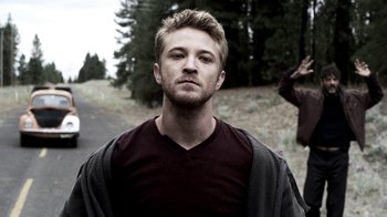 Movie still from “Z Nation” (2014), created by Karl Schaefer – A man with a beard is standing on the side of the road; Close Up shot, Low angle