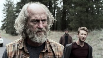 Movie still from “Z Nation” (2014), created by Karl Schaefer – A man with long white hair and a gray beard; Medium shot, Over the shoulder angle